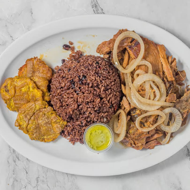 Shredded pork with sautéed onions, red rice and beans, fried plantains, and green sauce.