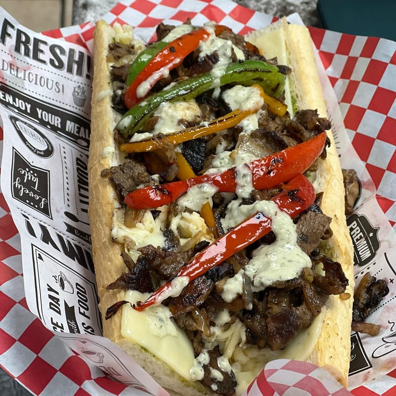 A delicious Philly cheesesteak with grilled peppers, onions, and sauce on a hoagie roll.
