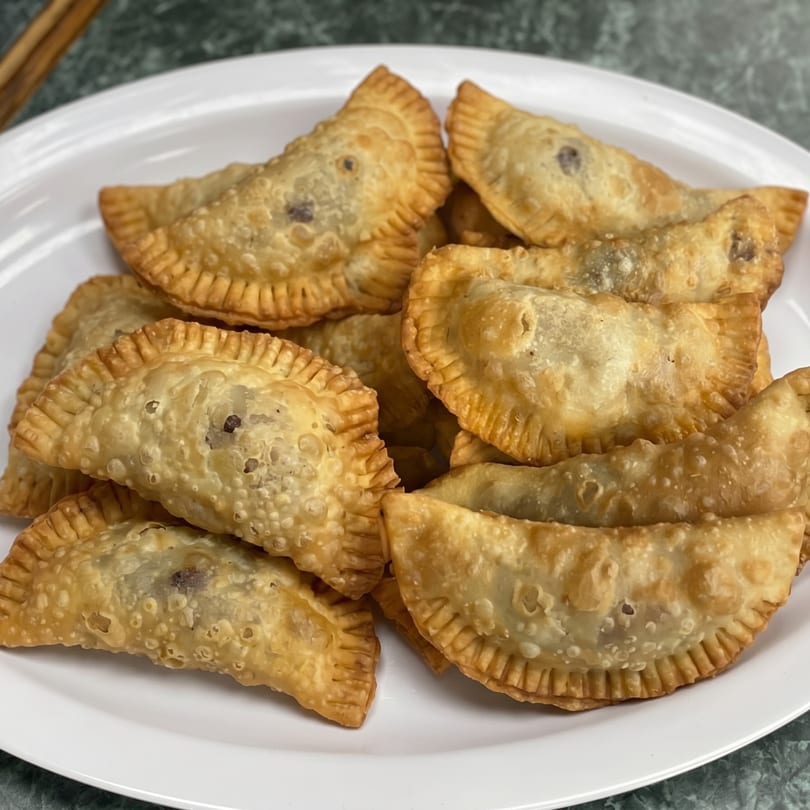 A white plate piled high with golden-brown, crispy empanadas, some with visible dark fillings.