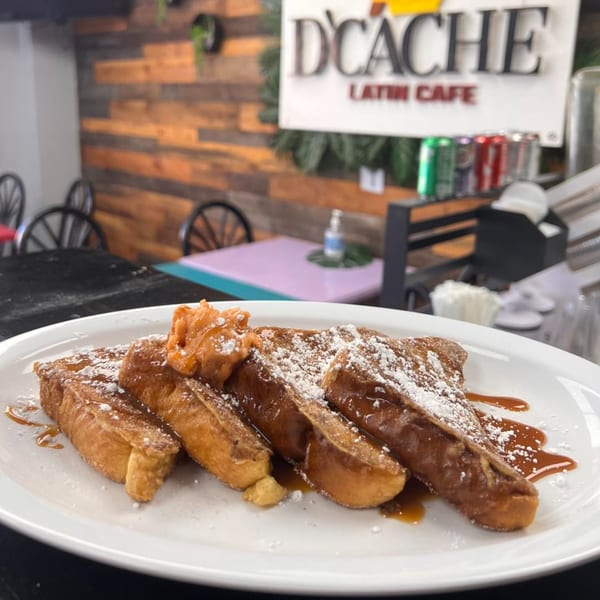 French toast with powdered sugar and syrup on a white plate at D'Cache Latin Cafe.
