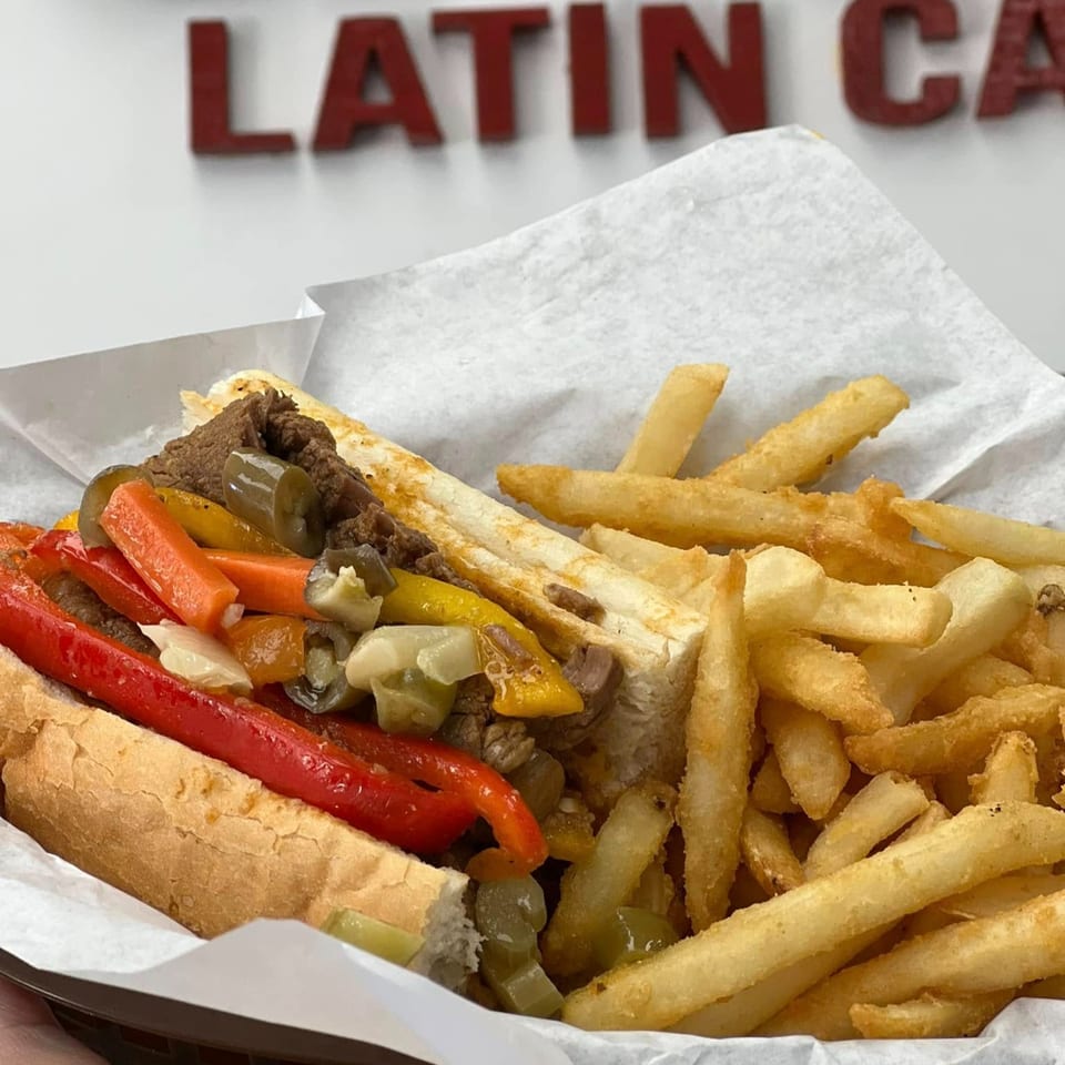 Cheesesteak sandwich with red and yellow peppers, mushrooms, and onions, served with golden fries.