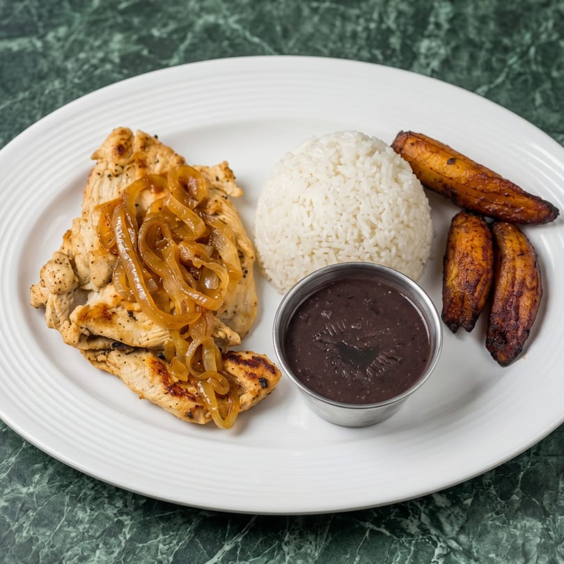 Grilled chicken with caramelized onions, white rice, black beans, and fried plantains on a white plate.