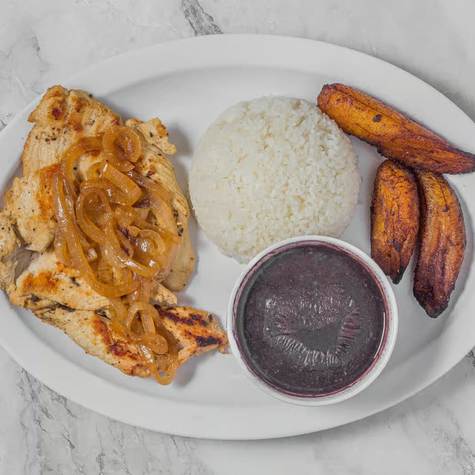 Grilled chicken with caramelized onions, white rice, black beans, and fried plantains on a white plate.